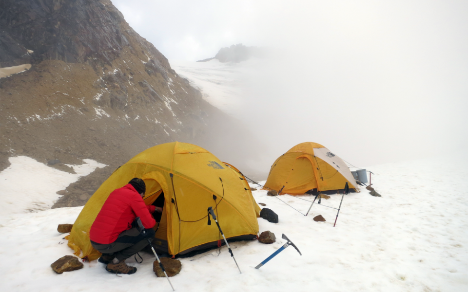 man reaching into yellow tent on snowy mountain
